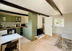 Eine kleine Küche mit Mikrowelle, Herd und Schränken. Es gibt einen Essbereich mit Tisch und Stühlen sowie einen Fernseher auf einem Schrank.