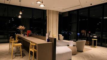 A modern bar area with seating, a counter, and large windows offering a city view.