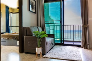 A modern living room with a grey sofa, a small potted plant, and a view of a balcony with a railing. - WCC The Base Central Pattaya (Bang Lamung)