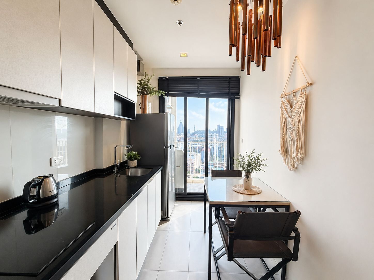 A modern kitchen with a black countertop, stainless steel appliances, and a city view through large windows.