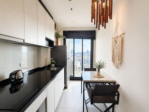 A modern kitchen with a black countertop, stainless steel appliances, and a city view through large windows. - WCC The Base Central Pattaya (Bang Lamung)