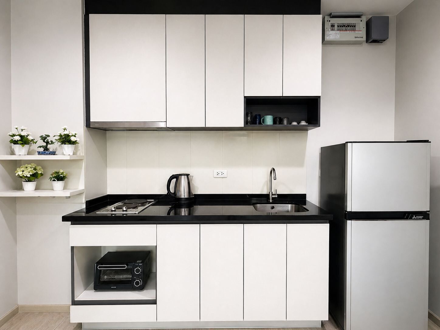 A modern kitchen with white cabinets, a black countertop, a kettle, a toaster, and a refrigerator.