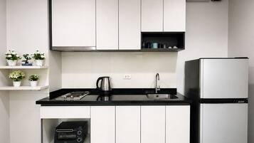 A modern kitchen with white cabinets, a black countertop, a kettle, a toaster, and a refrigerator.