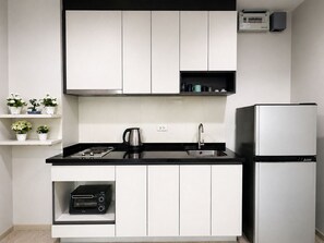 A modern kitchen with white cabinets, a black countertop, a kettle, a toaster, and a refrigerator. - WCC The Base Central Pattaya (Bang Lamung)