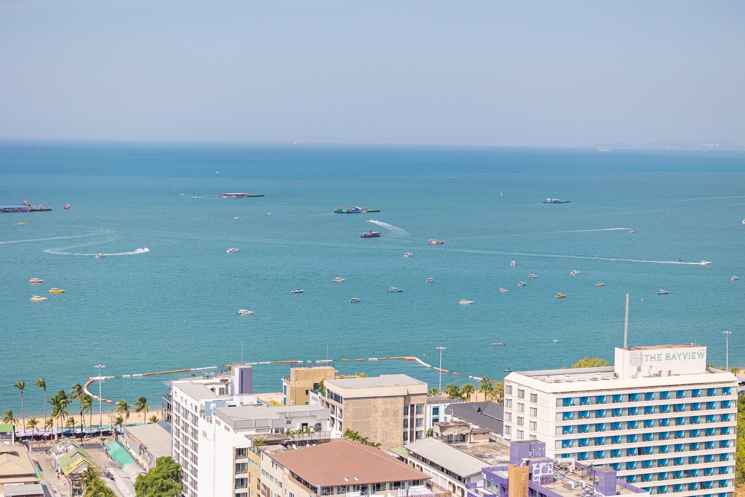 Un paysage urbain côtier avec un port de plaisance rempli de bateaux, des immeubles dotés de balcons donnant sur la mer et un hôtel appelé « The Bayview », qui offre une vue sur l’océan.