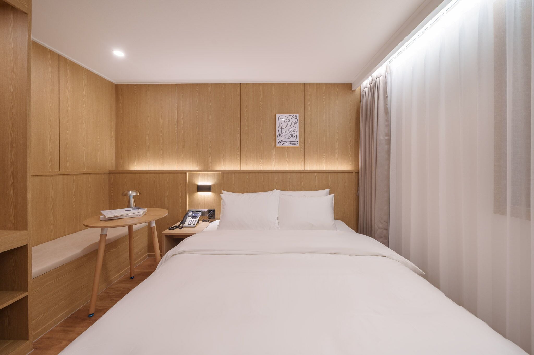 A hotel room with a bed, bedside table, lamp, and a phone.