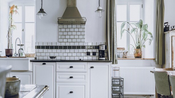 Una cocina con armarios blancos, salpicadero de azulejos y una cafetera.