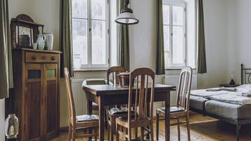 A room with a wooden table, chairs, a radiator, a bed, and a window with curtains.