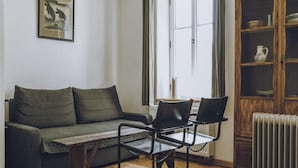 Ein Zimmer mit einer Couch, zwei Sesseln, einem Heizkörper und einem Schrank.