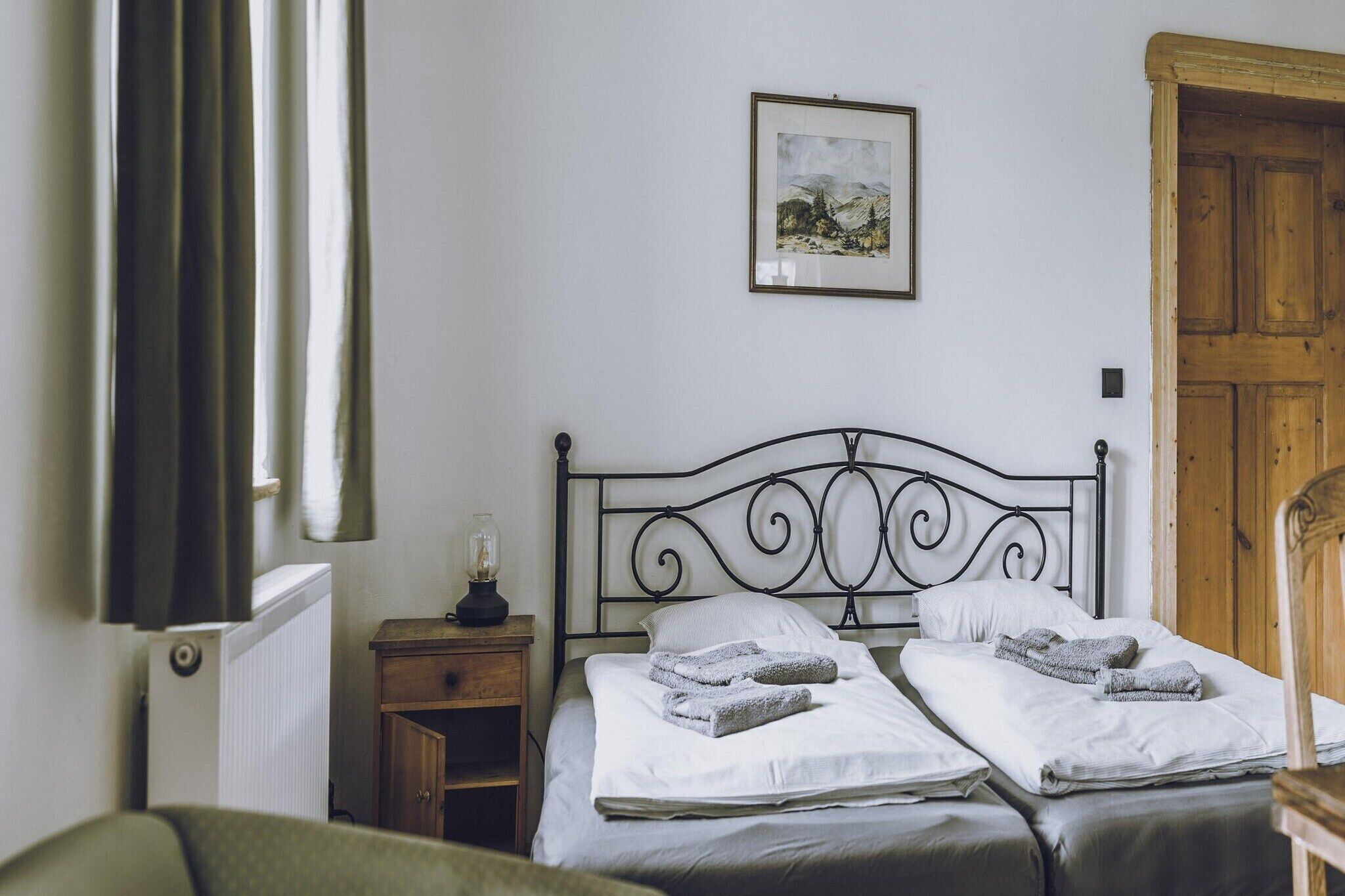 A bedroom with two beds, a nightstand with a lamp, a wooden door, and a framed picture on the wall.