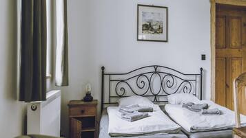 A bedroom with two beds, a nightstand with a lamp, a wooden door, and a framed picture on the wall.