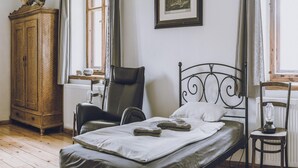 Ein Zimmer mit einem Bett, einem Holzschrank, einem Sessel und einem gerahmten Bild an der Wand.