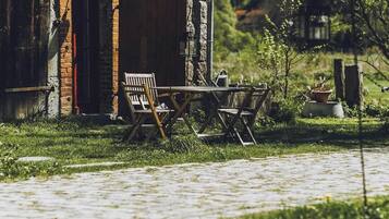 A rustic stone building with a brick archway, a wooden bench, and a table set outdoors.