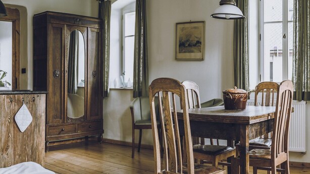 Una stanza con un tavolo da pranzo in legno, sedie, un armadietto con uno specchio, un lampadario e una finestra con tende.