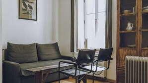 Una stanza con un divano, due poltrone, un termosifone e un mobile contenitore con stoviglie.