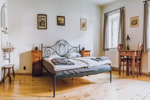 Ein Schlafzimmer mit einem Metallbettgestell, Holzbeistelltischen, einem Schreibtisch mit Stuhl und einem Fenster mit Vorhängen.