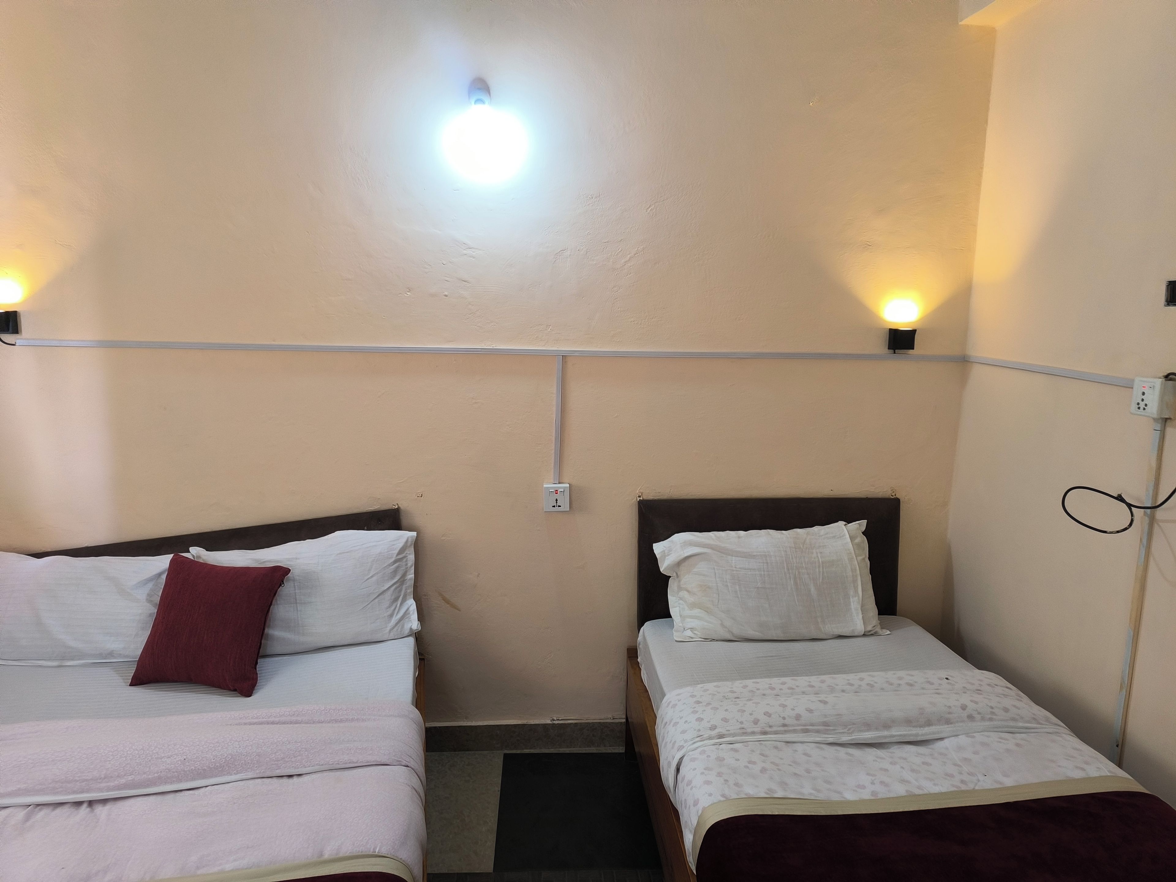 Una habitación pequeña y sencilla con dos camas, una lámpara en el techo y un enchufe en la pared.