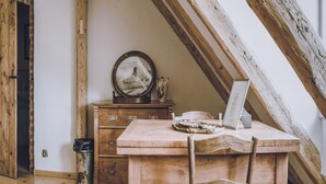 Un bureau en bois rustique, sur lequel se trouvent un ordinateur portable, un cadre avec une photo et un vase, dans un coin d’une pièce dont les poutres en bois sont apparentes.