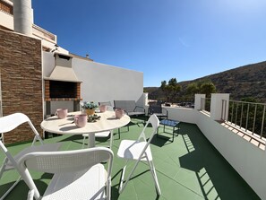 A rooftop terrace with a round table, chairs, and a barbecue area.