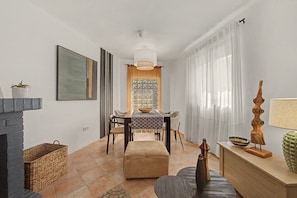 A modern living room with a fireplace, a dining area with a table and chairs, and a large window with curtains.
