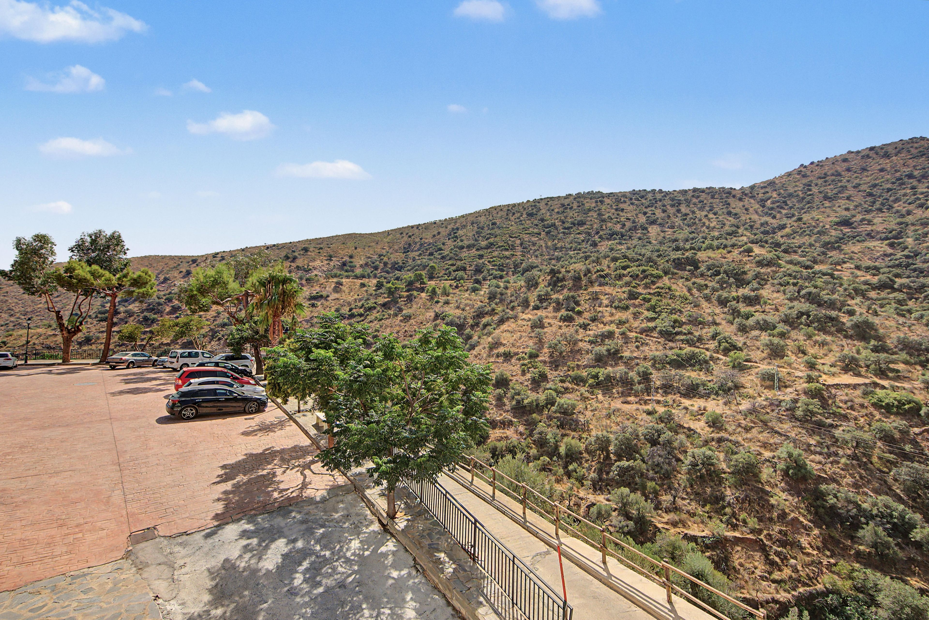 Un espace de stationnement avec des voitures, un chemin pavé et une colline à la végétation clairsemée.