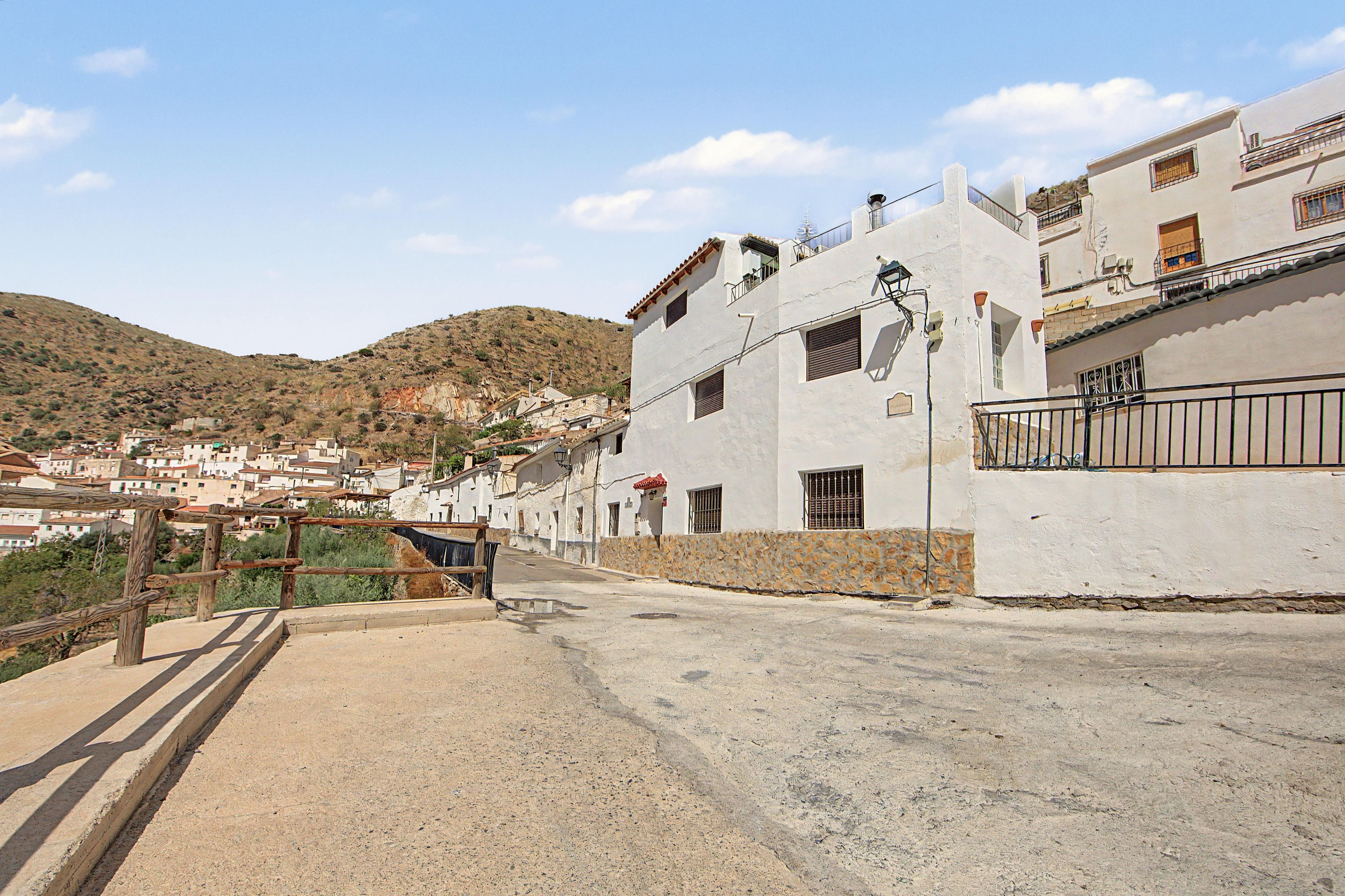 Una calle con edificios blancos, un muro de piedra y una valla de madera.