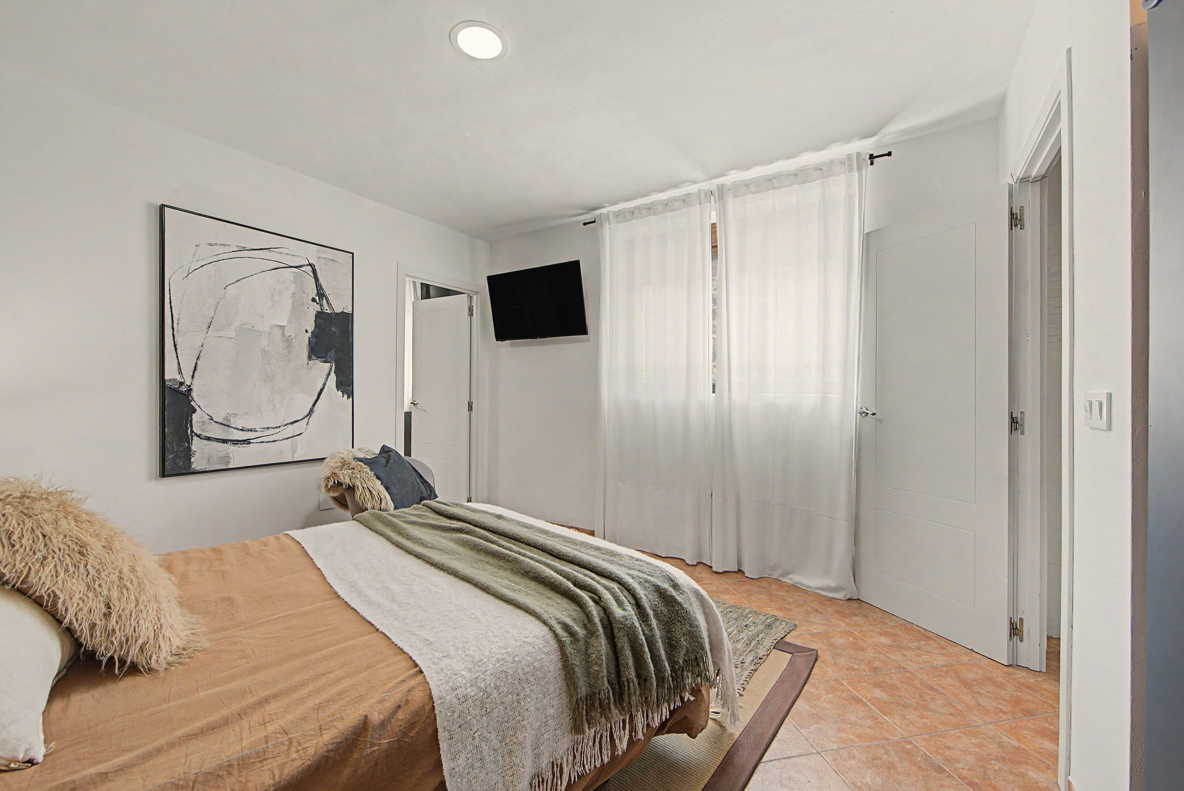Een slaapkamer met een bed, een televisie, een schilderij en een deur.