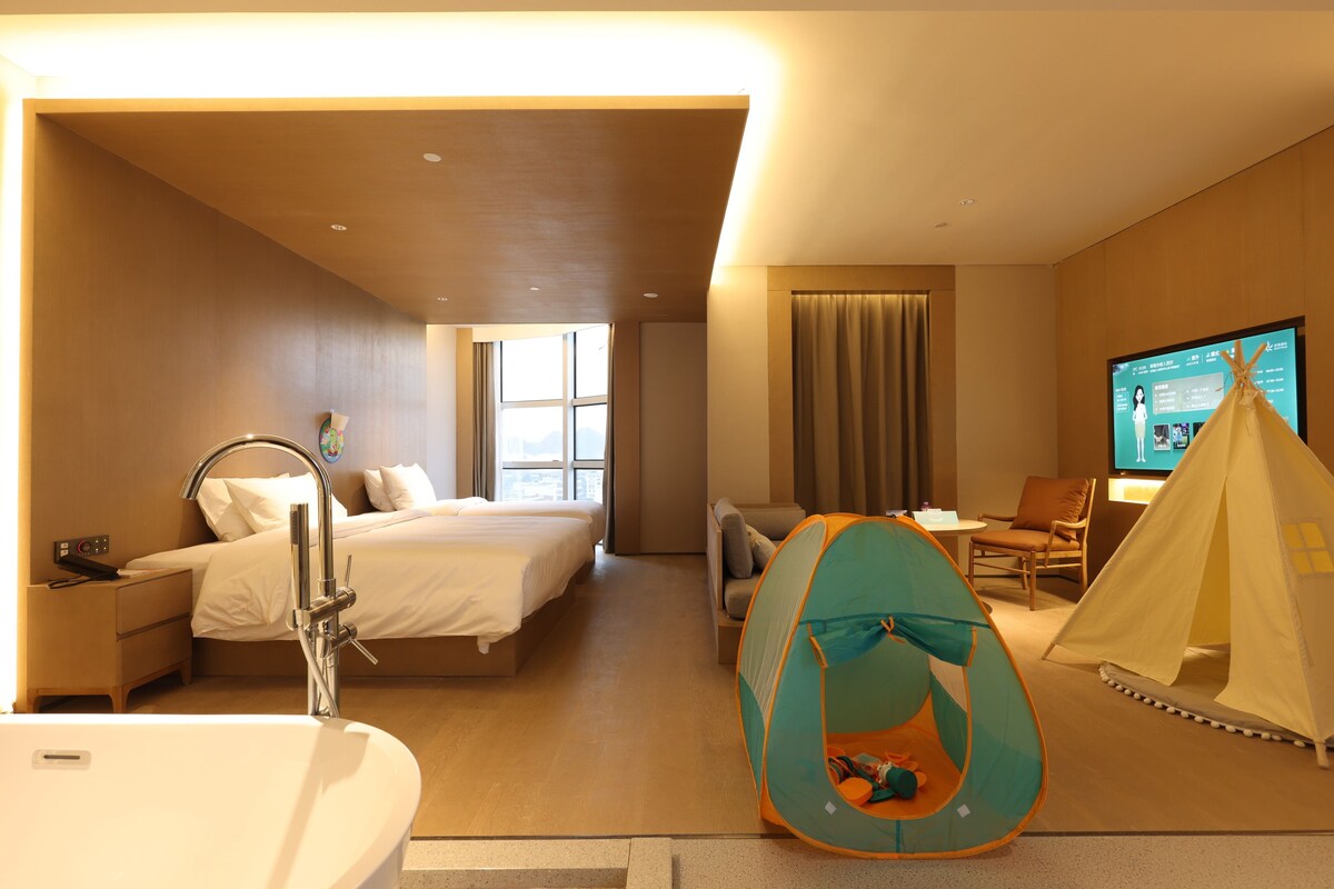 A hotel room with a bed, a bathroom, a seating area, and a tent.