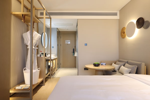 A hotel room with a large bed, a round table with a bowl, a sofa, a mirror, and a wardrobe.