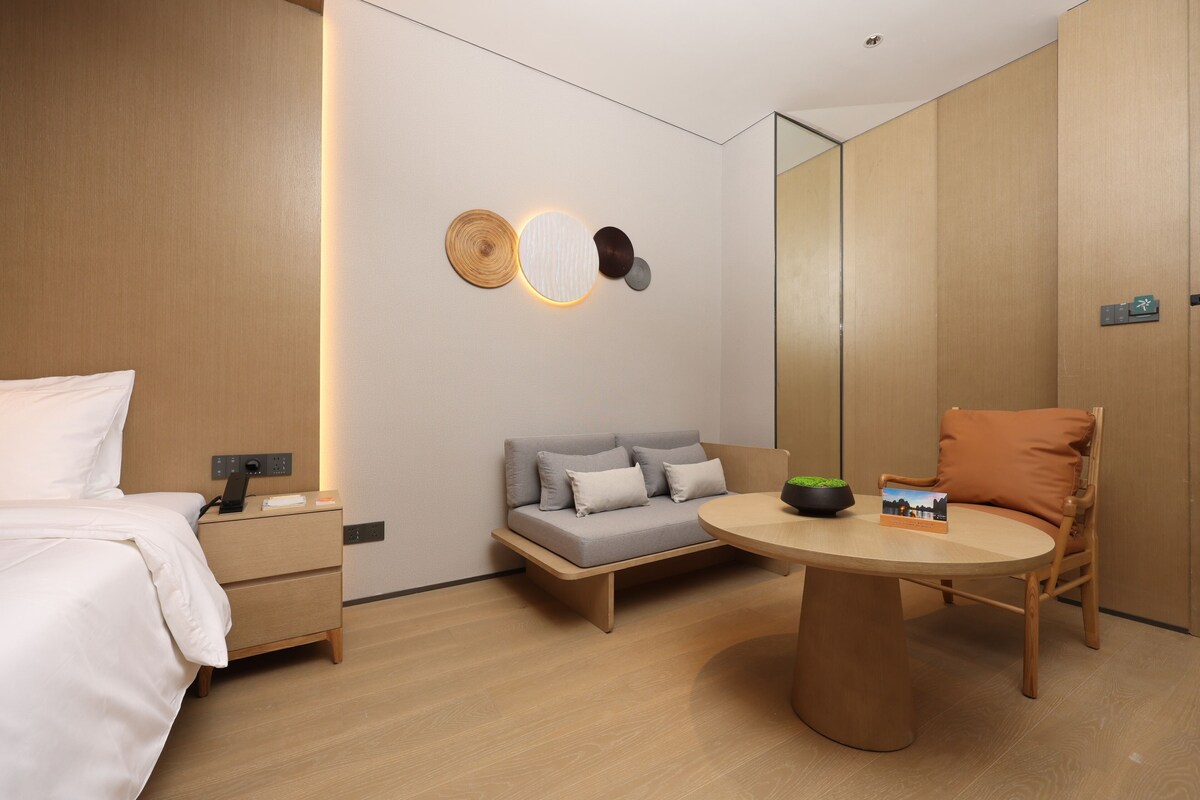 A modern hotel room with a bed, a sofa, a dining table, and a mirror.