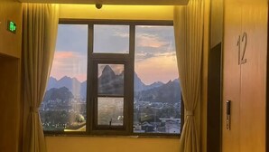 Una habitación con un amplio ventanal que ofrece vistas a montañas y un paisaje urbano.