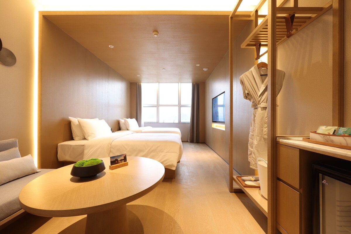 A hotel room with a bed, a round table, a sofa, a robe hanging, and a view of the outside.