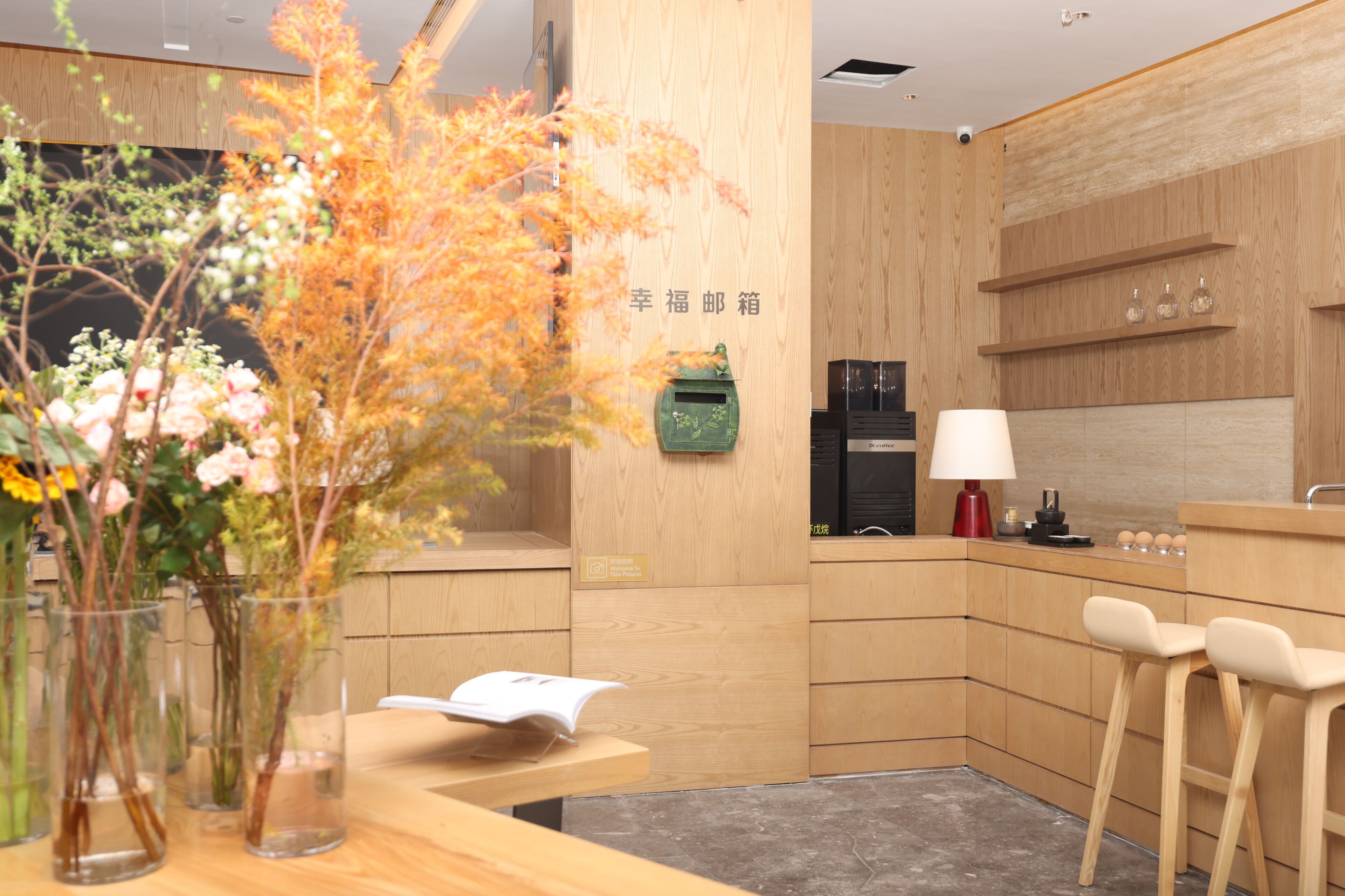 Un espace d’accueil moderne avec un comptoir de réception en bois, un vase rempli de fleurs et un panneau fixé au mur.
