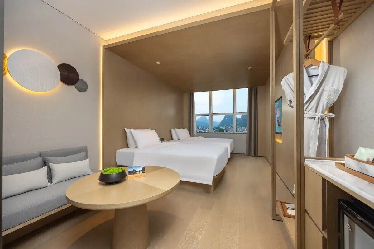 A hotel room with a bed, a sofa, a round table, and a view of the city.