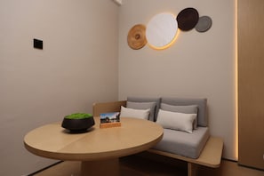 A modern room with a round wooden table, a grey sofa with cushions, and a wall-mounted light fixture.