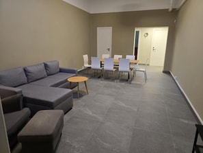 Una sala de estar con un sofá seccional gris, una mesa redonda para café y una zona de comedor con una mesa de madera y sillas blancas.