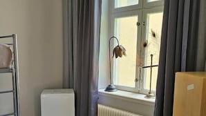 Una habitación con radiador, ventana con cortinas, cubierta para radiador y un armario de madera.
