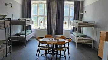 A dormitory room with bunk beds, a round table, chairs, and a radiator.