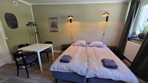 Una habitación con dos camas, una mesa, sillas y una planta colgante.