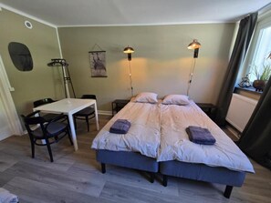 Una habitación con dos camas, una mesa, sillas y una planta colgante.