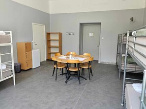 Una habitación con literas, una mesa redonda con sillas, un armario pequeño y una puerta.