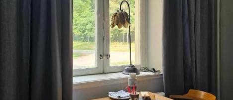 Ein Zimmer mit Tisch, zwei Stühlen, einem Heizkörper und einem Fenster mit Vorhängen.