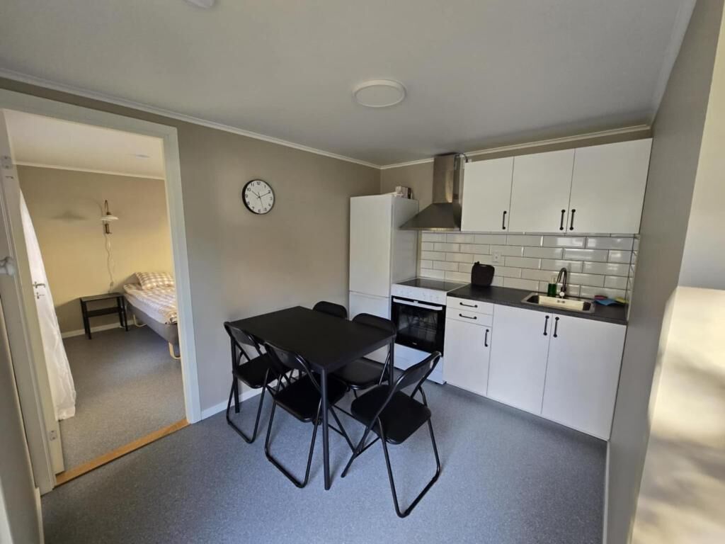 Ett kompakt kök med vita skåp, en svart bänkskiva och en matplats med ett bord och stolar.