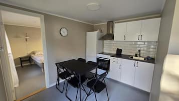 Ett kompakt kök med vita skåp, en svart bänkskiva och en matplats med ett bord och stolar.
