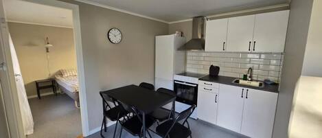 A compact kitchen with white cabinets, a black countertop, and a dining area with a table and chairs.