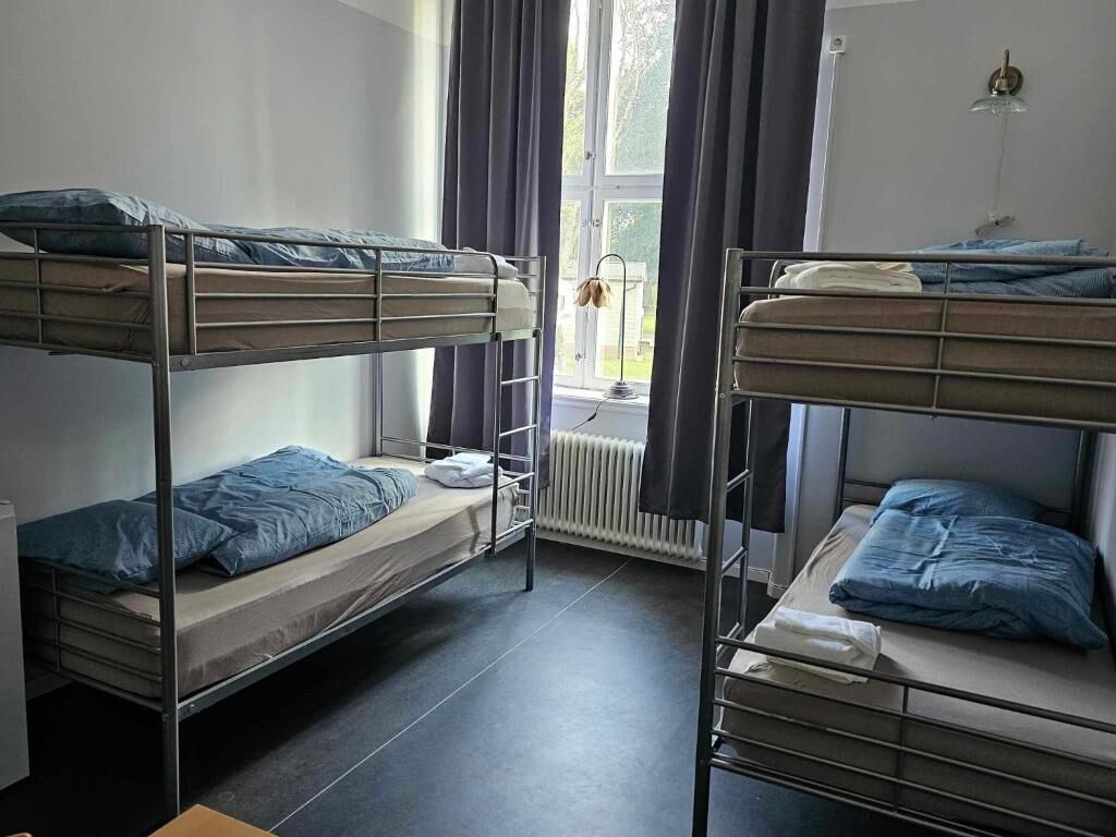 A room with bunk beds, a radiator, a window with curtains, and a lamp.