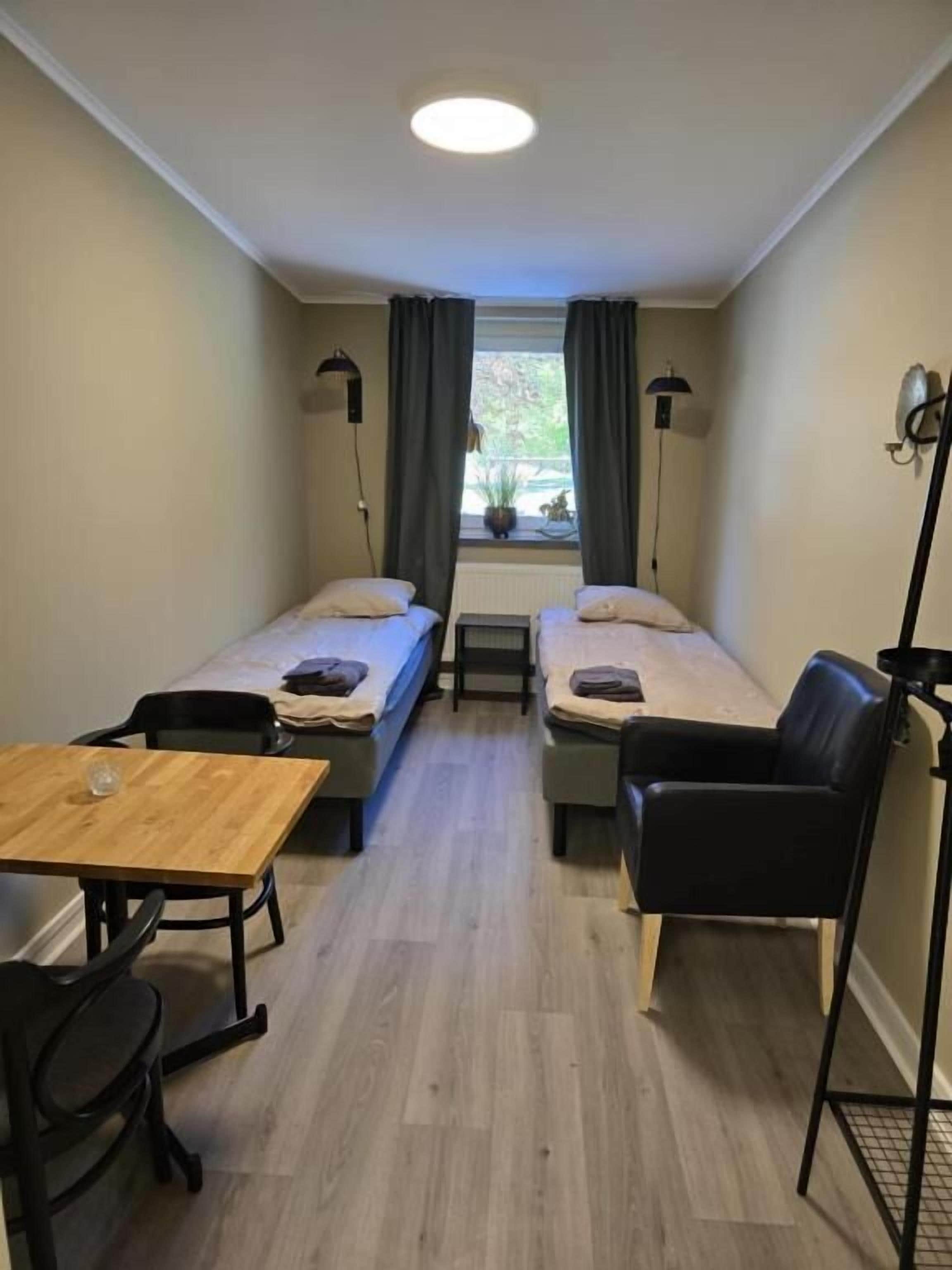 Quarto pequeno e compacto com duas camas de solteiro, uma mesa de madeira e uma cadeira.