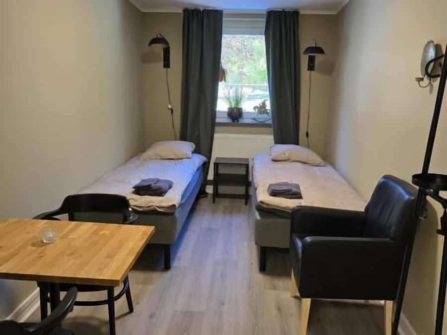 A small, compact room with two single beds, a wooden table, and a chair.
