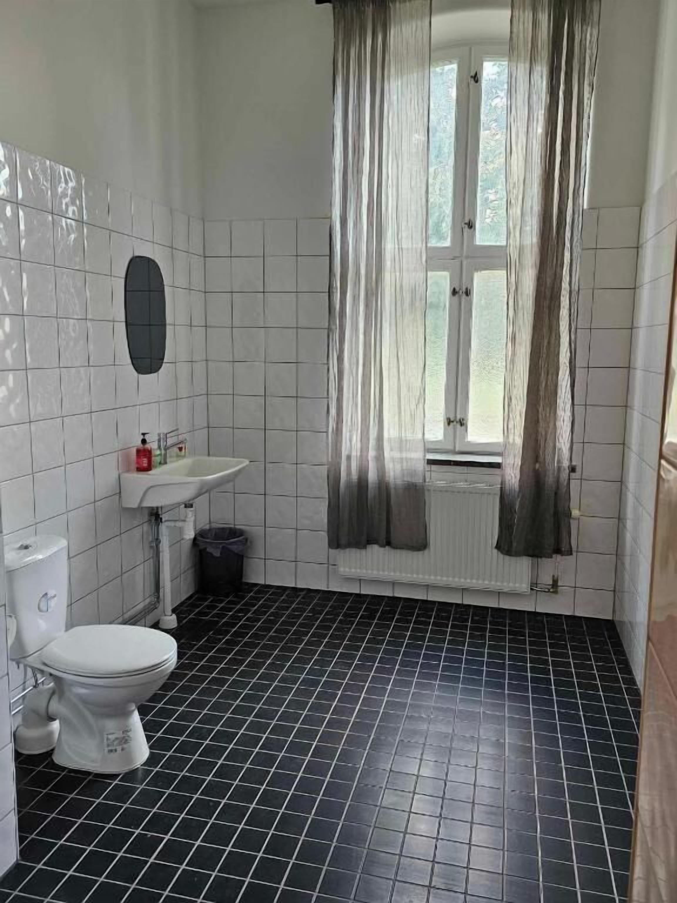 A bathroom with a toilet, sink, and window with curtains.