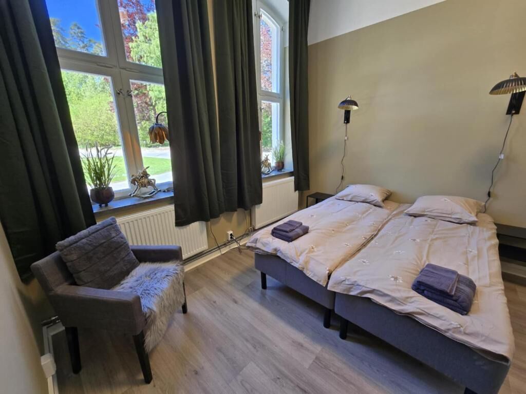 Un dormitorio con dos camas, una silla y una ventana con cortinas.